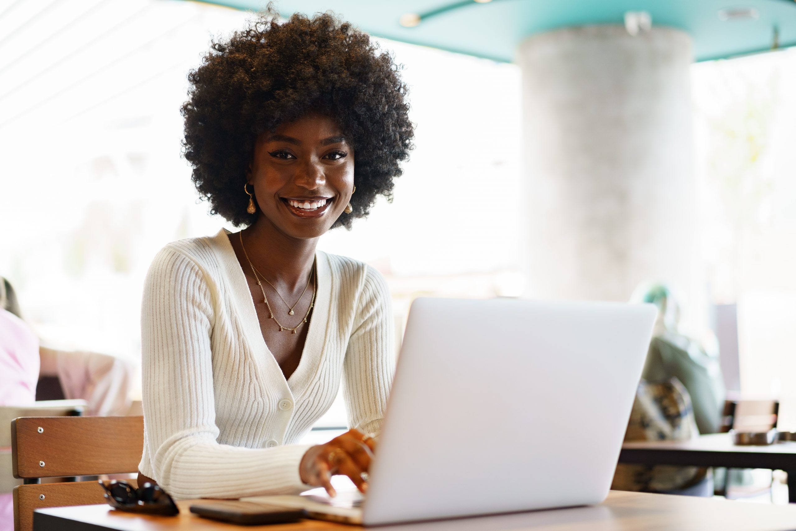 Smiling young african woman sitting with laptop in cafe, portrait
